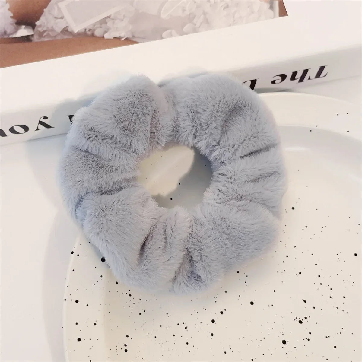 Un élastique pour cheveux en tricot flou gris clair est exposé sur une assiette blanche à côté d'une boîte.