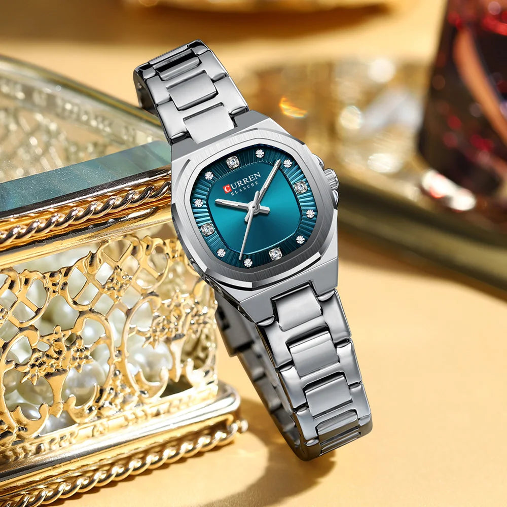 Silberfarbige Quarz-Armbanduhr mit blauem Zifferblatt und Metallarmband auf einer verzierten Goldbox.