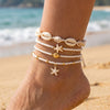 A stack of white and gold starfish conch bracelets worn on a wrist against a beach background.