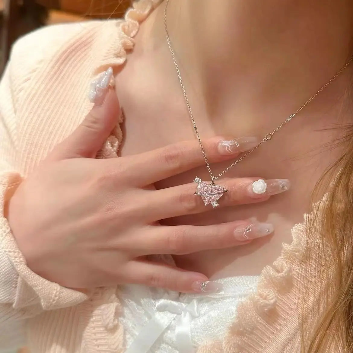 A close-up of a woman wearing a pink heart zircon clavicle necklace with delicate gold chain and sparkling stones.