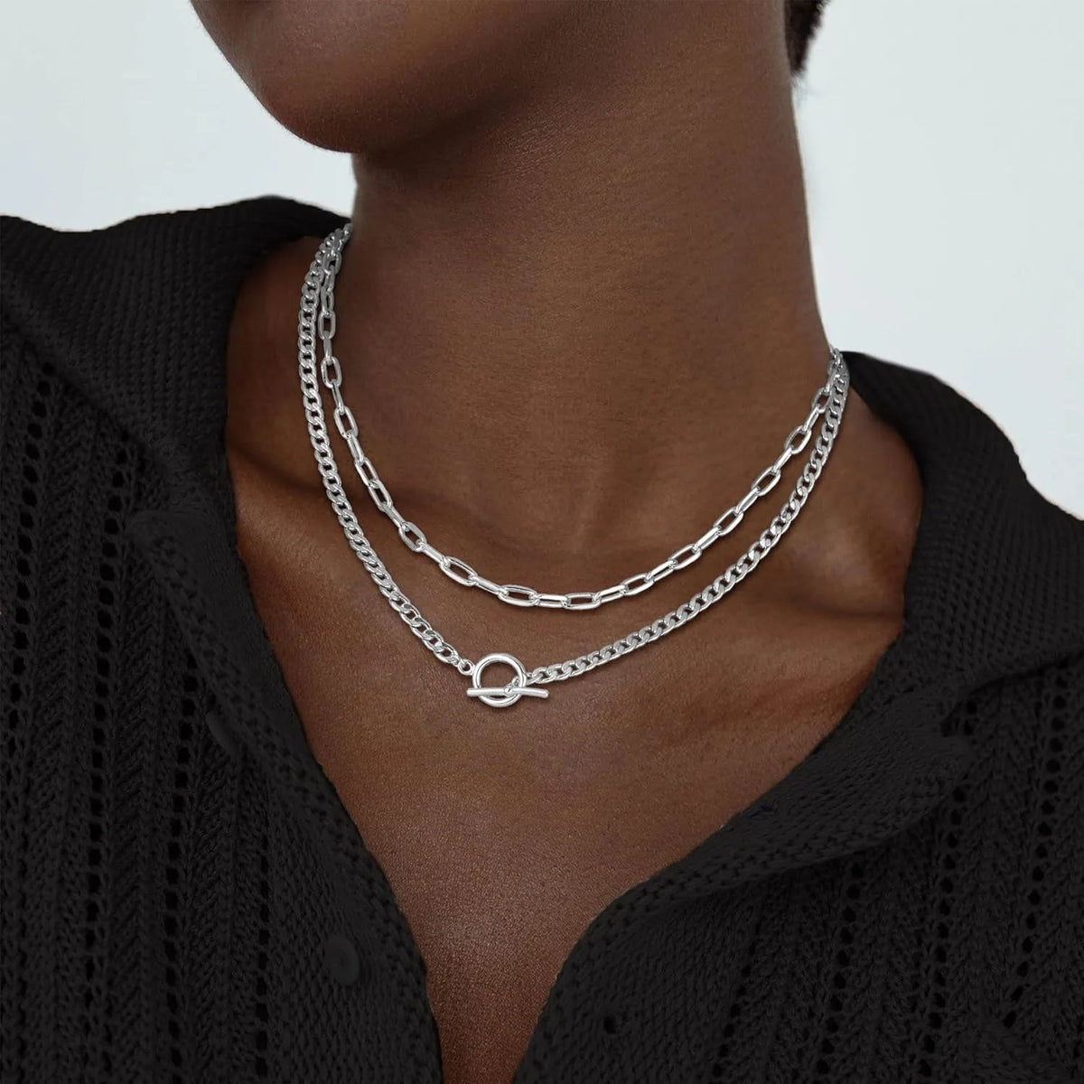 A close-up of a gold layered Cuban link necklace worn around the neck against a dark garment.