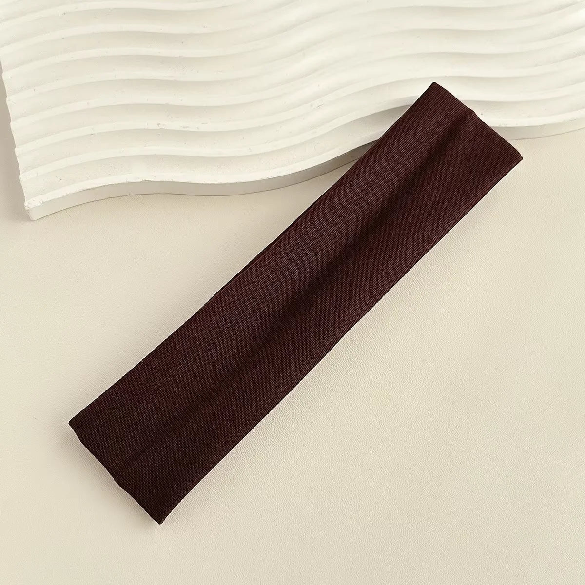 A dark brown fabric headband is shown diagonally against a light background with wavy lines.