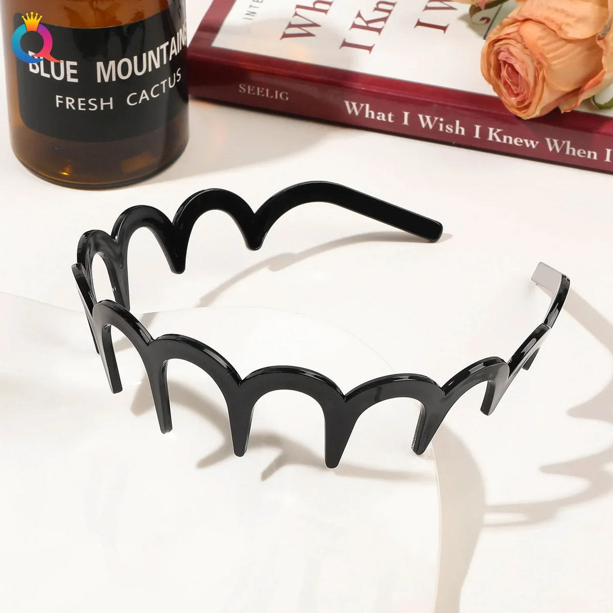 Black fashion acetate toothed headbands displayed on a white surface next to a book and a bottle.