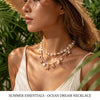 A close-up of a woman wearing a delicate pearl and starfish necklace against a backdrop of green foliage.