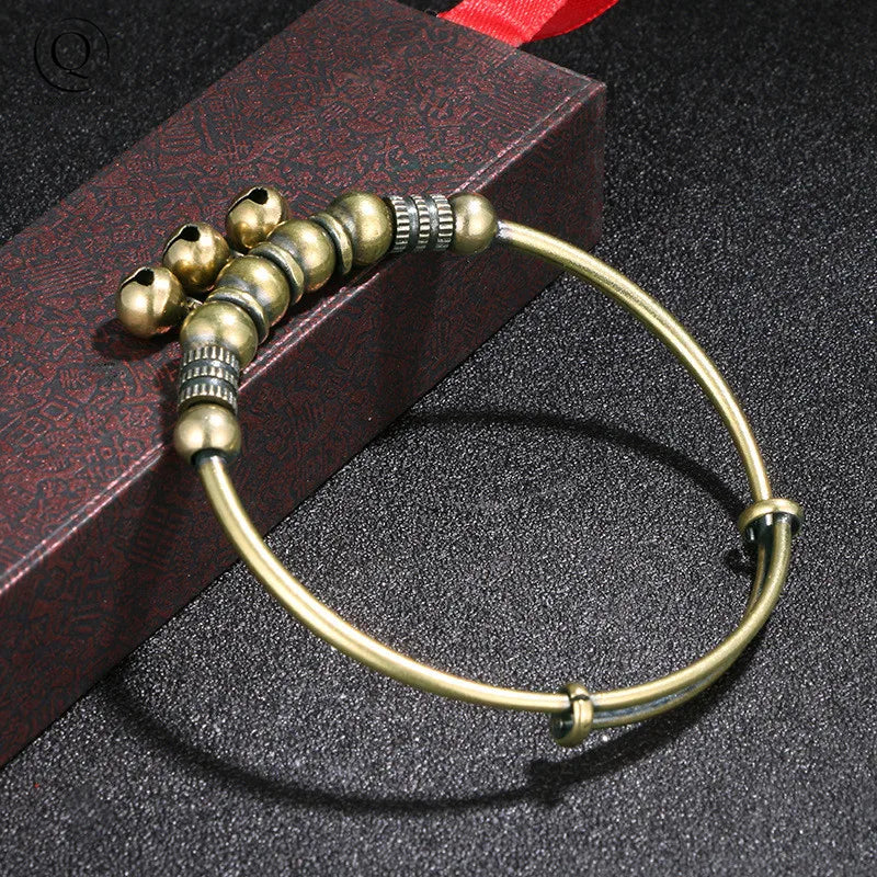 A vintage brass bell charm bracelet is displayed on a dark surface next to a red box.