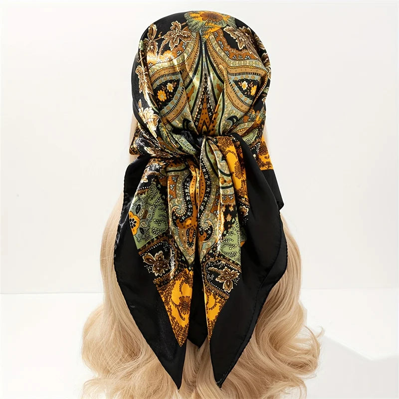 A black and gold patterned satin silk scarf tied in a bow, displayed on blonde hair.