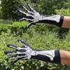 A hand wearing black and white skeleton print gloves is shown against a green outdoor background.