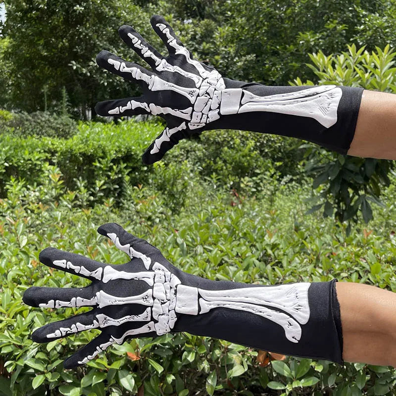 A hand wearing black and white skeleton print gloves is shown against a green outdoor background.