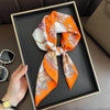 An orange and white silk scarf tied in a bow is displayed in a black frame on a brown surface.
