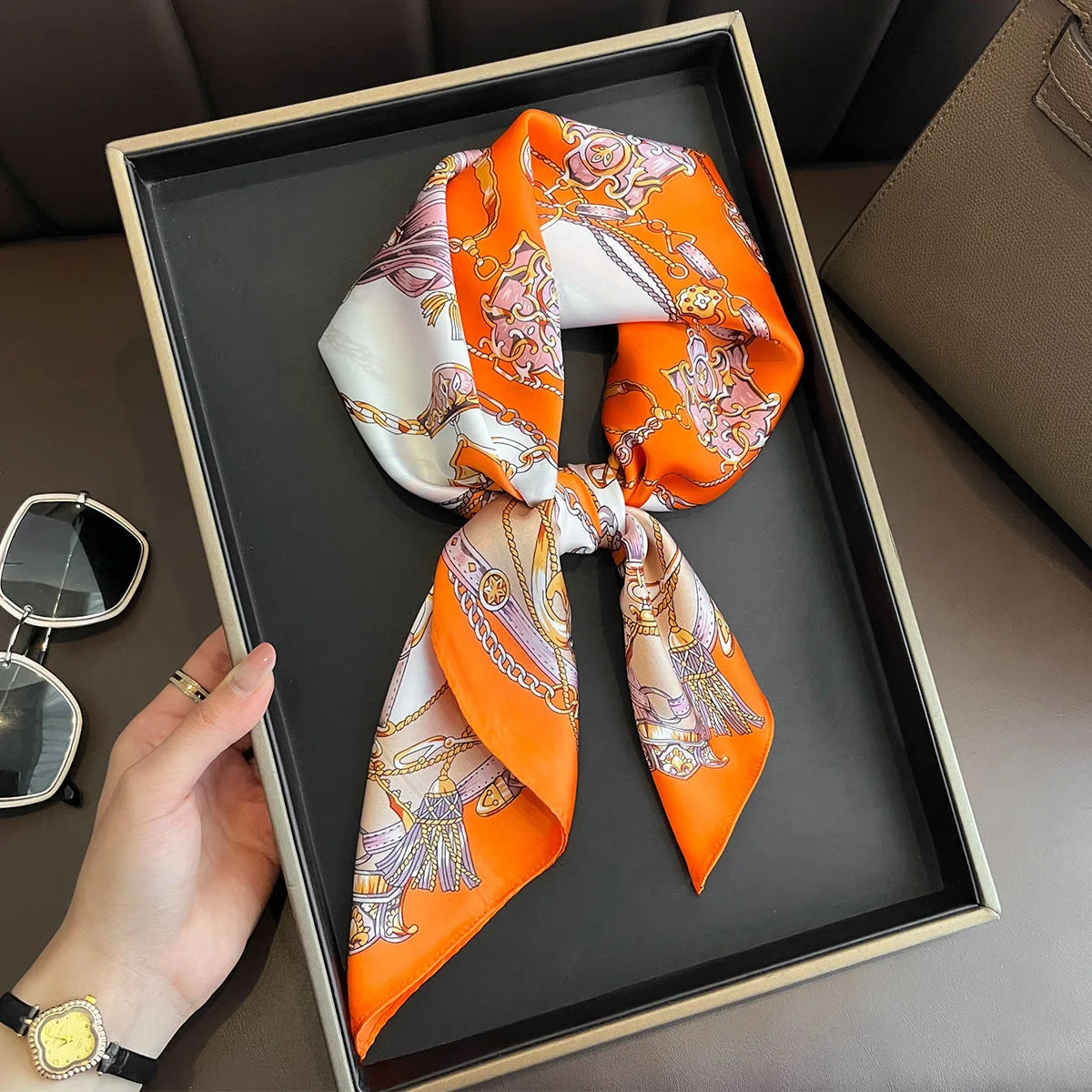 An orange and white silk scarf tied in a bow is displayed in a black frame on a brown surface.