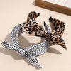A leopard print retro bow hairband tied in a decorative knot, lying on a light surface.