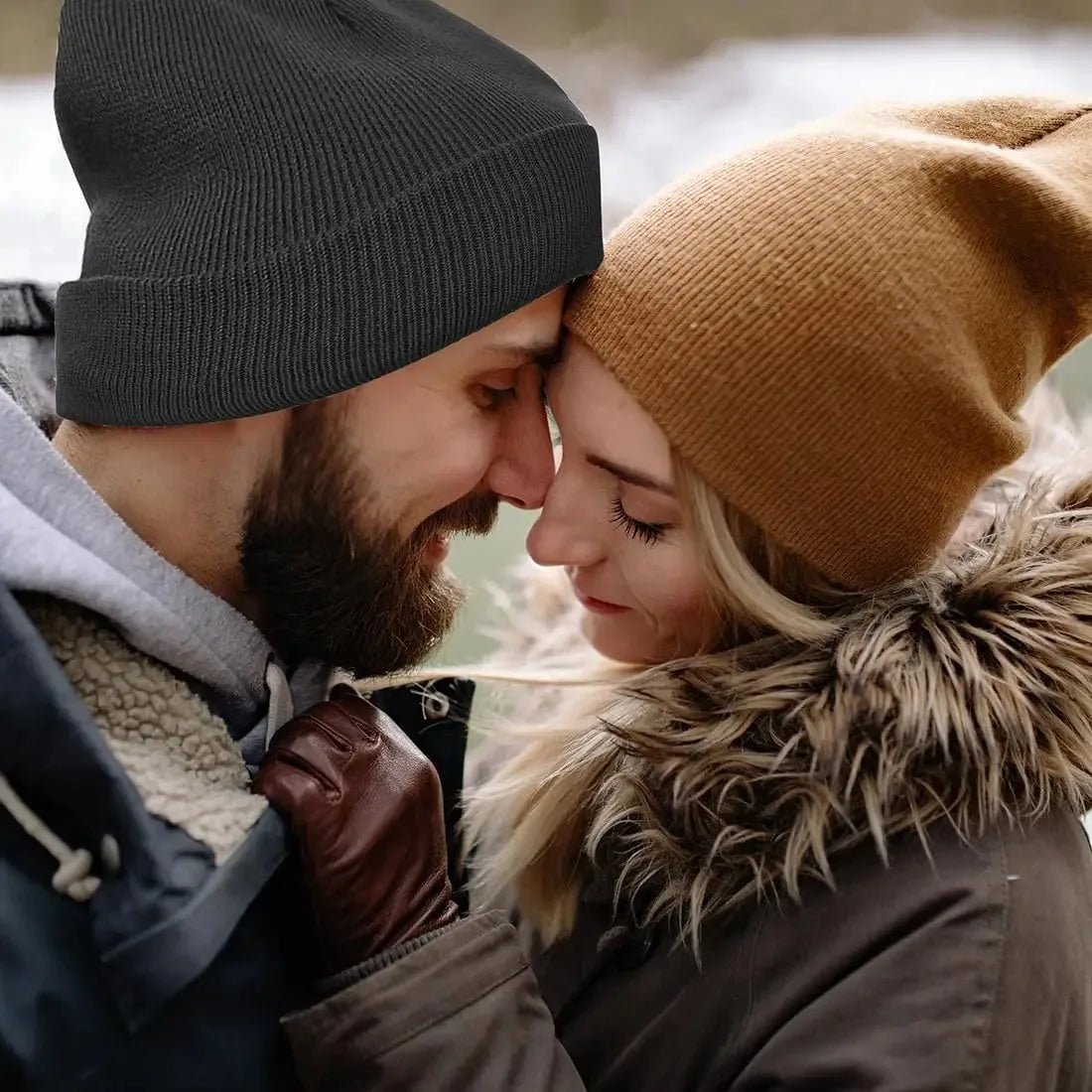 A close-up portrait of a couple kissing, focusing on their faces and knitted winter hats.