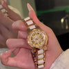 Una mano sostiene un elegante reloj de cuarzo con diamante dorado y correa blanca.