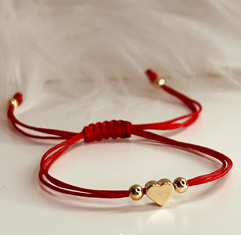 A red handmade baby heart bracelet with gold accents is displayed against a white background.