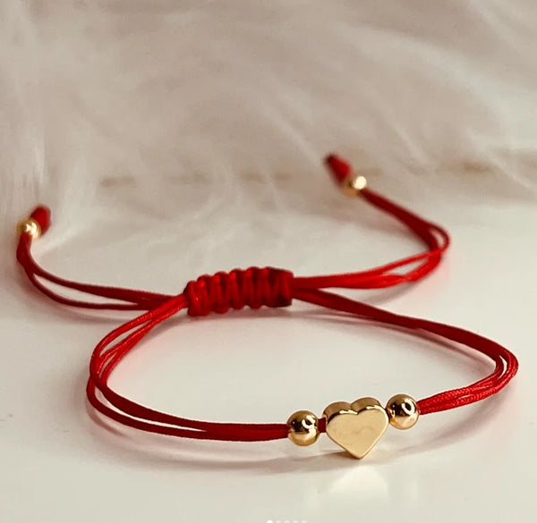 A red handmade baby heart bracelet with gold accents is displayed against a white background.