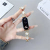 A hand holds a black smartwatch with a gold strap featuring diamond four-leaf clover accents.