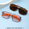 Un par de gafas de computadora cuadradas anti-luz azul en tonos ámbar y naranja sobre una superficie azul claro.