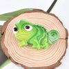 A small, bright green lizard figurine is placed on a cross-section of wood.