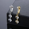 A pair of gold-toned fashion belly button rings with clear and gold-colored stones displayed on a black box.