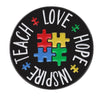 An enamel lapel pin featuring the words TEACH LOVE INSPIRE HOPE formed by colorful puzzle pieces.