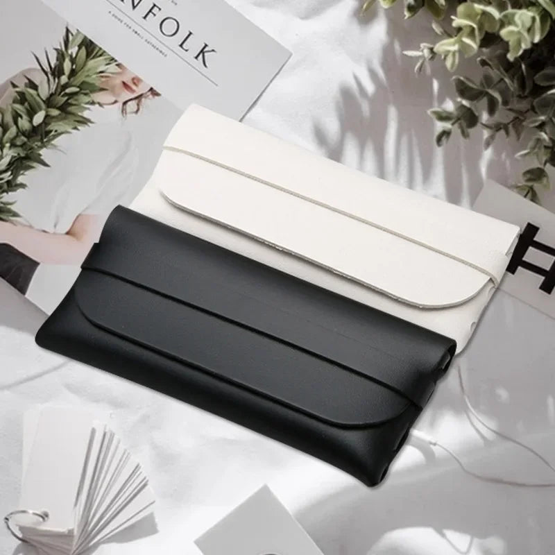 A black leather eyeglass case is shown open next to a white case on a light surface.