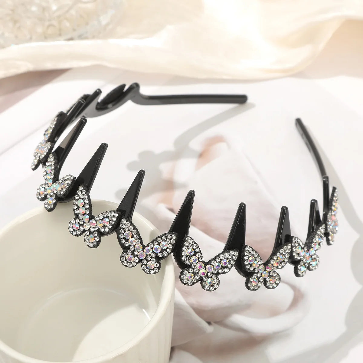 A black rhinestone butterfly hair accessory is displayed on a white surface next to a white cup.