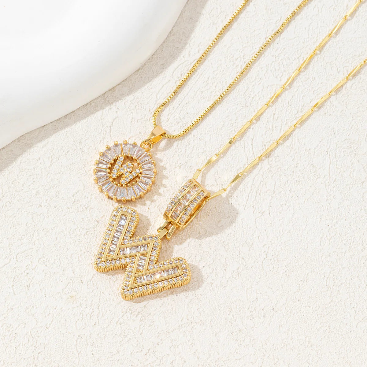 Gold necklace set featuring CZ crystal pendants shaped like letters and lightning bolts.