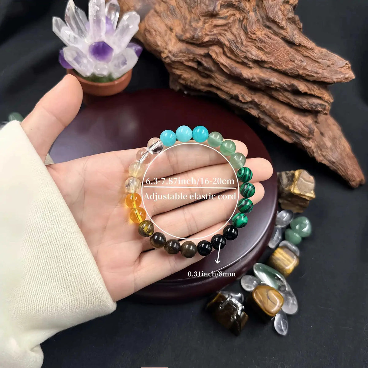 A hand holds a bracelet made of natural stone beads in various shades of blue, green, and brown.