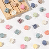 A collection of colorful mini flower hair clips in shades of pink, purple, blue, and cream arranged on a wooden surface.