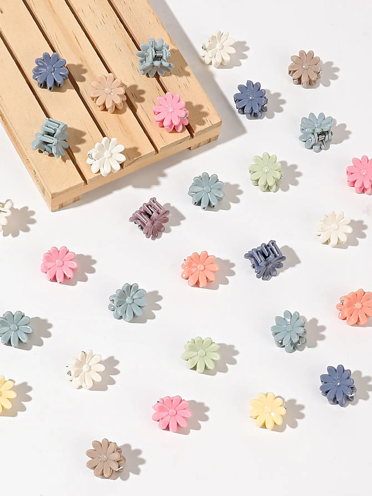 A collection of colorful mini flower hair clips in shades of pink, purple, blue, and cream arranged on a wooden surface.