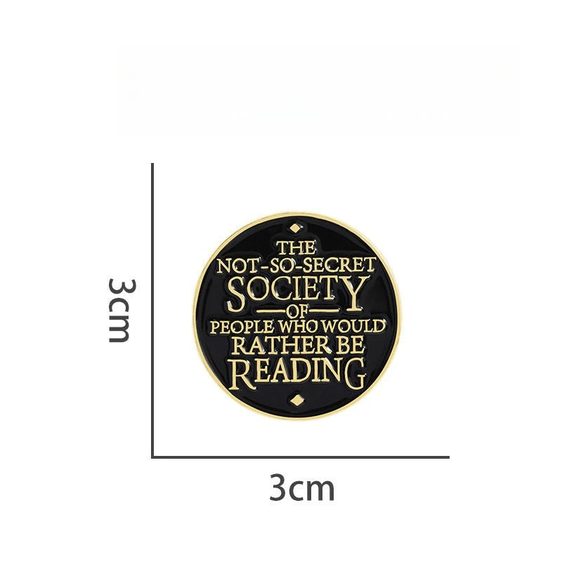 A round black lapel pin featuring the text The Not-So-Secret Society of People Who Would Rather Be Reading in gold lettering.