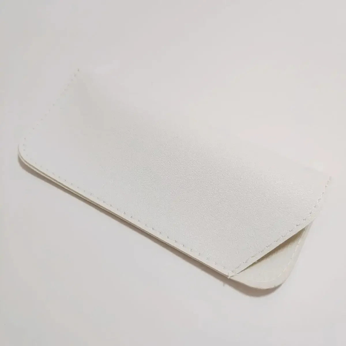 A white PU leather glasses case folded and lying on a light surface.