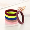 A stack of ten colorful elastic hair ropes in shades of red, green, yellow, blue, purple, and pink on a white surface.