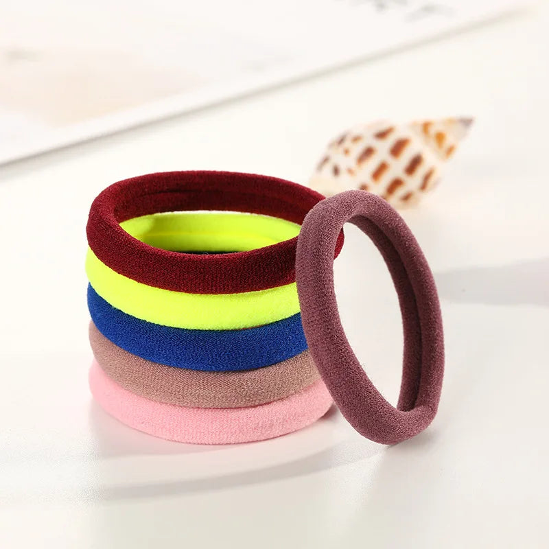 A stack of ten colorful elastic hair ropes in shades of red, green, yellow, blue, purple, and pink on a white surface.