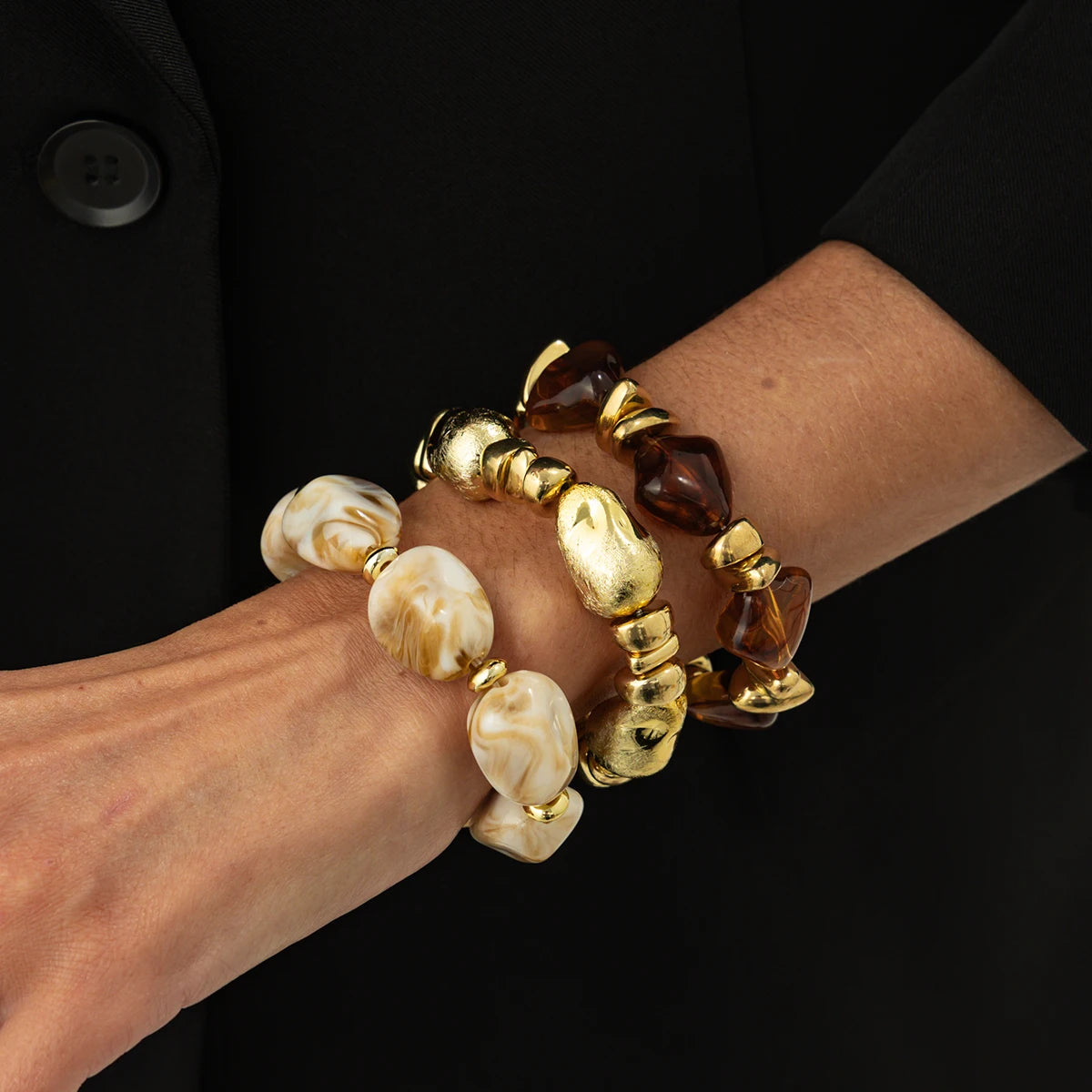 Un set de bracelets charm vintage en résine acrylique bohème avec des perles ambre et dorées sur un poignet.