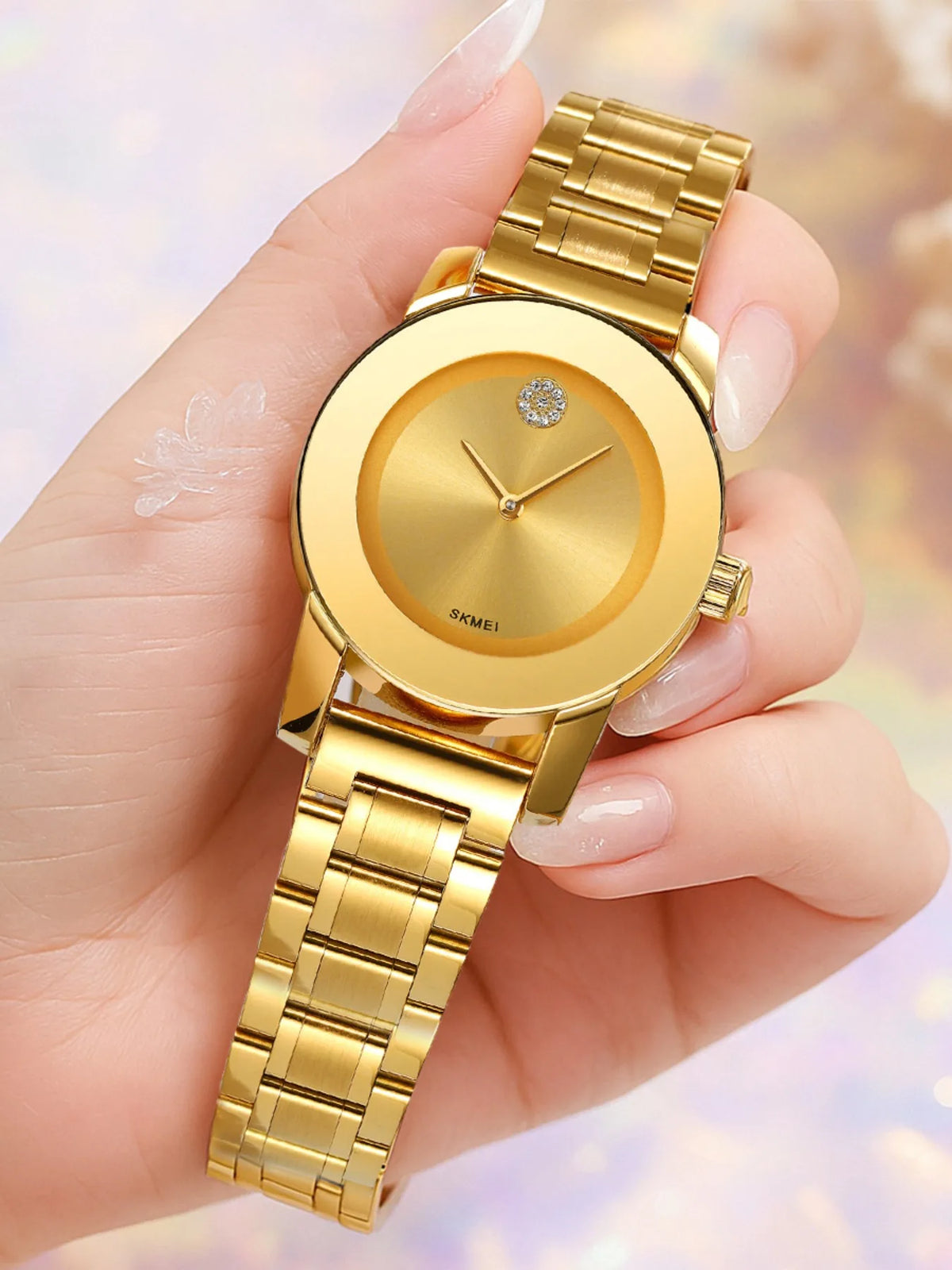Una mano sostiene un reloj de cuarzo dorado con caja redonda y pulsera de eslabones dorados.