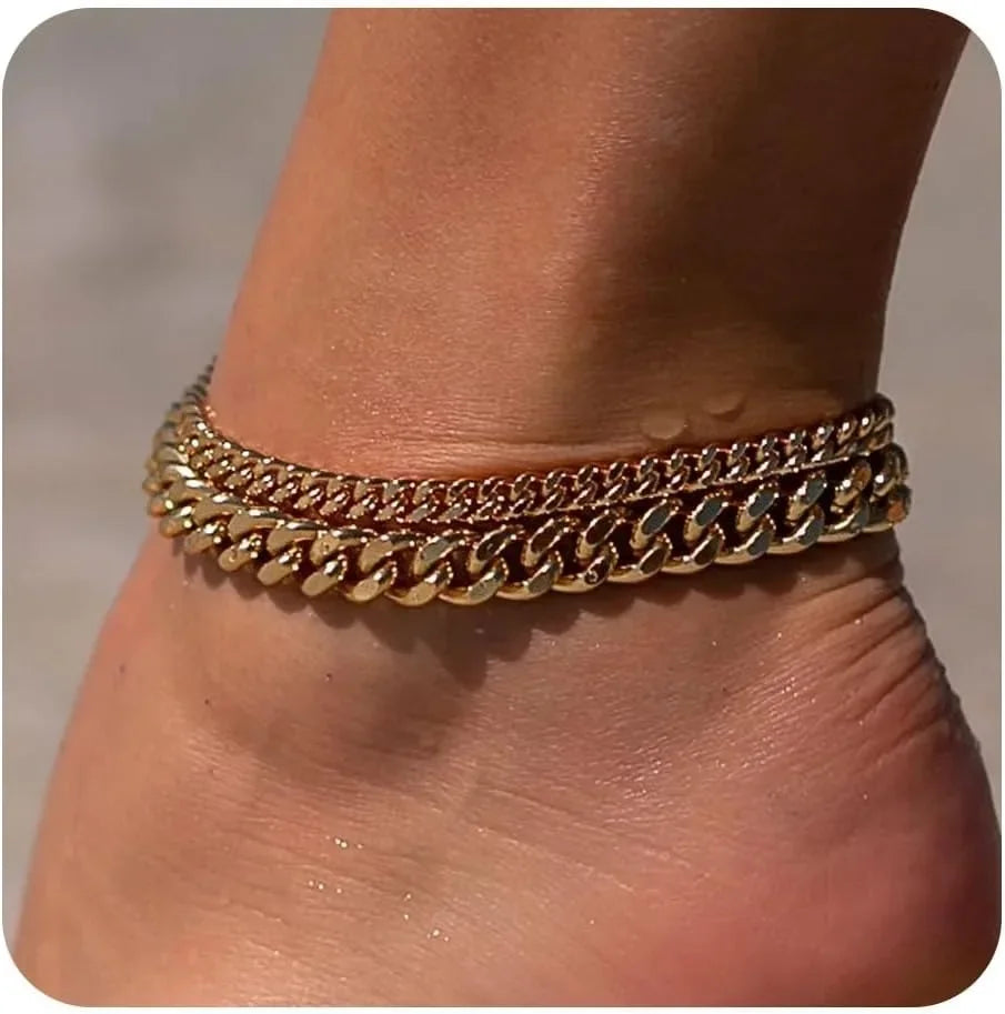 Gold plated minimalist Cuban link anklets worn around the ankle of a person.