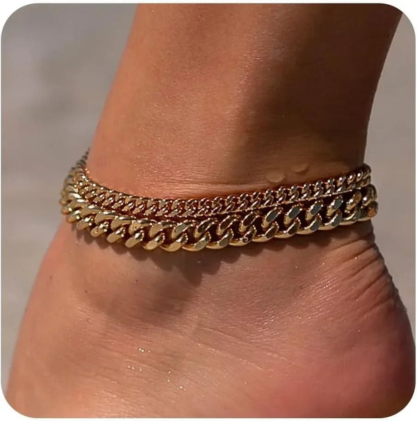 Gold plated minimalist Cuban link anklets worn around the ankle of a person.