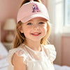 A smiling young girl wearing a pink unicorn letter baseball cap with a purple design.