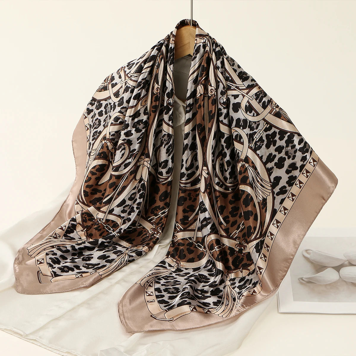 A square satin scarf featuring a leopard print design in shades of brown and black.