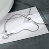 A sterling silver double heart charm bracelet displayed on a white card against a dark gray background.