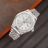 A silver-toned wristwatch with a white dial and date display is shown on a dark gray fabric.