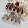 Two high-gloss amber hair clips are displayed on crumpled parchment paper.