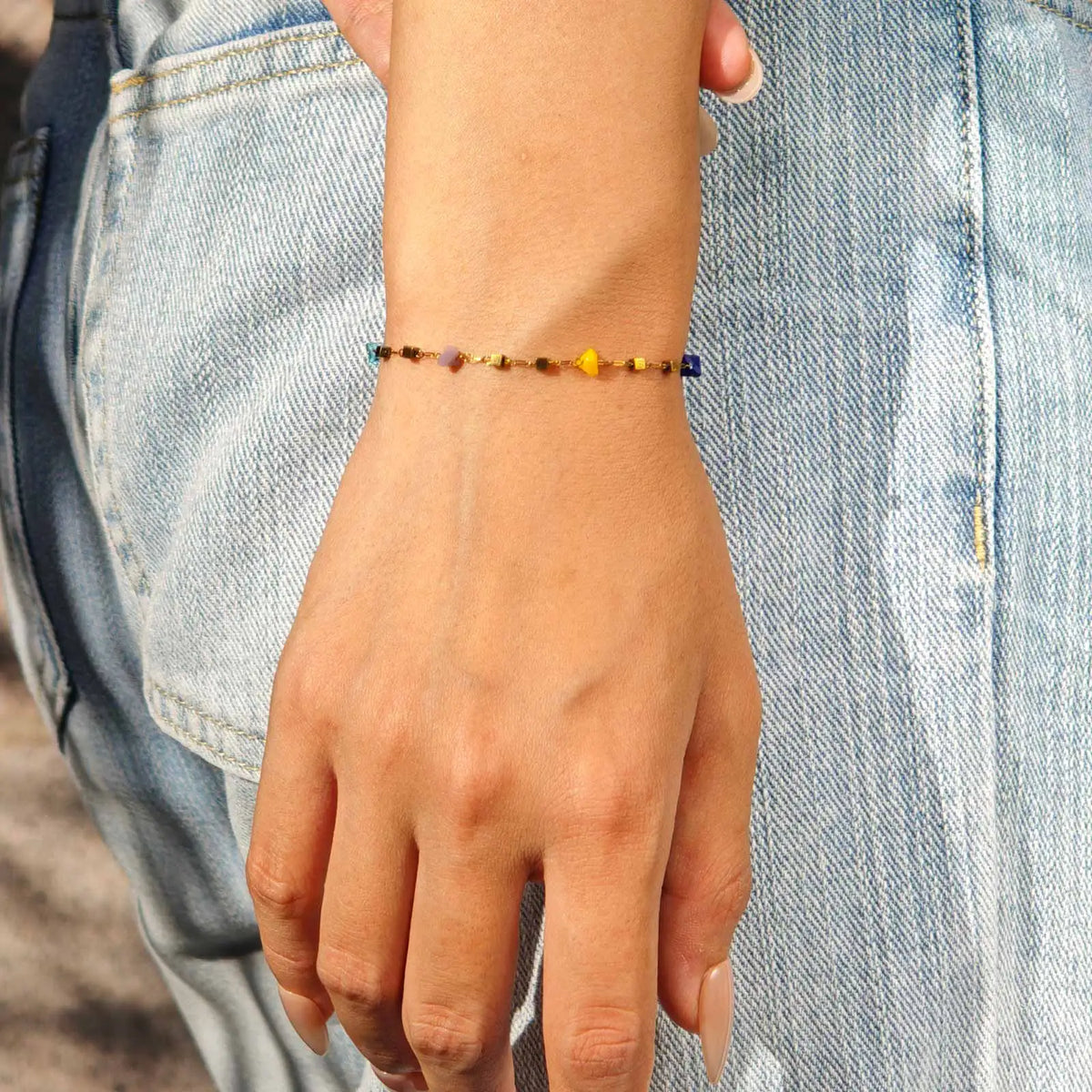 A hand wearing a colorful boho irregular stone choker necklace on a denim shirt.