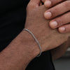 A close-up of a man's wrist wearing a silver stainless steel Cuban link bracelet.