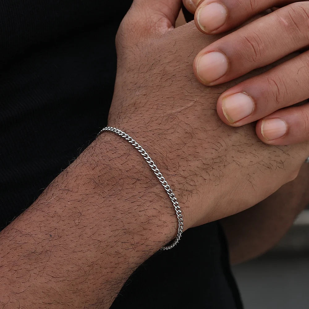 A close-up of a man's wrist wearing a silver stainless steel Cuban link bracelet.