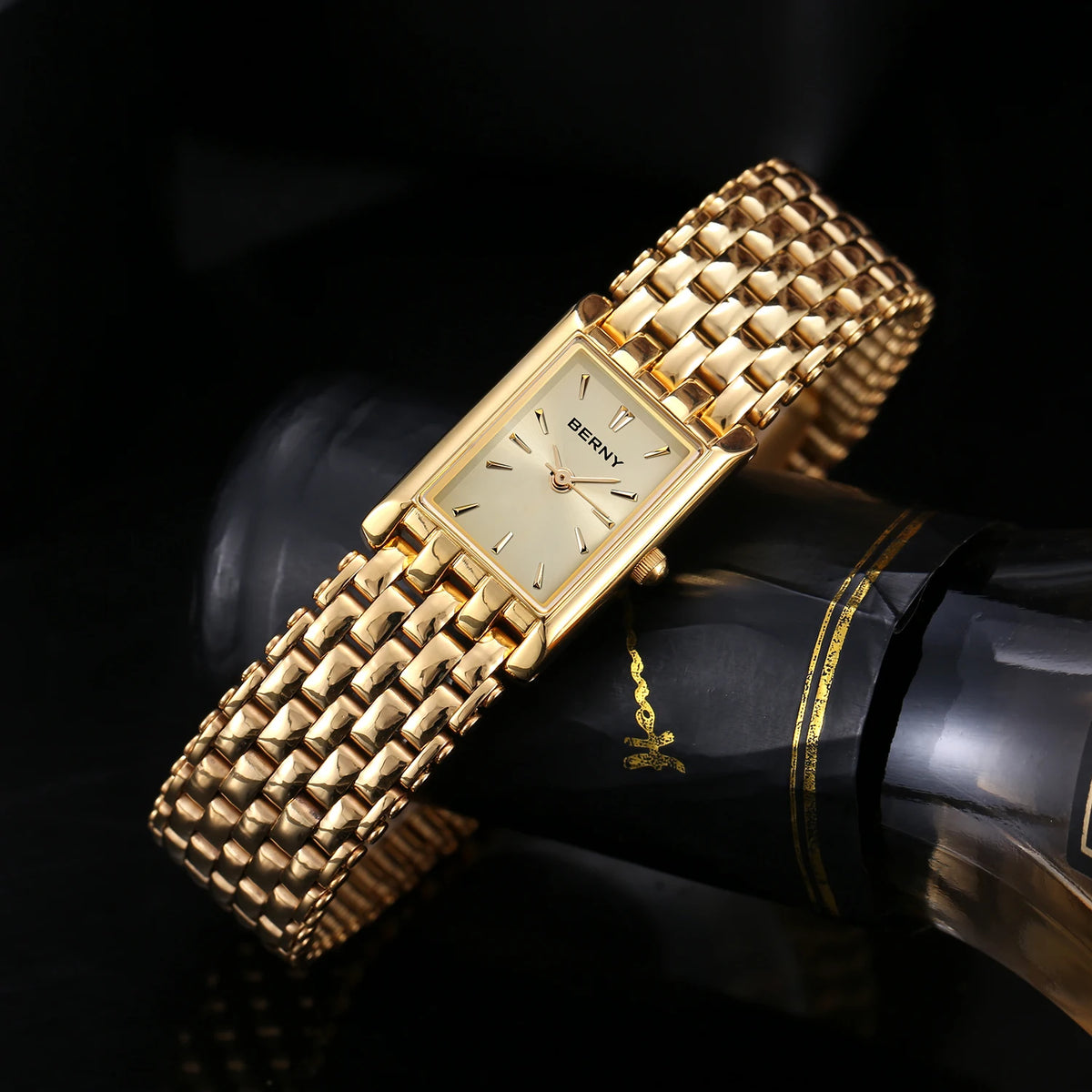 Gros plan d'une montre quartz pour femme plaquée or avec un bracelet doré texturé, posée sur une surface noire.
