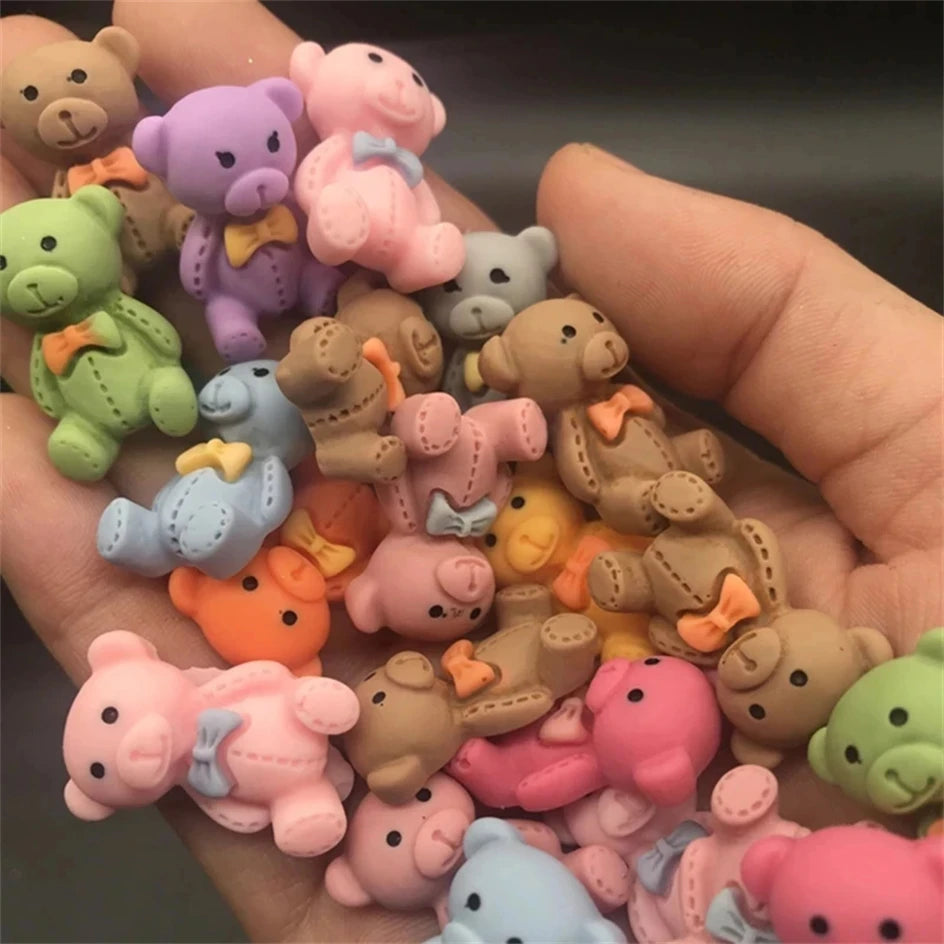 A hand holds a collection of 10 pink and beige resin nail art charms featuring cute bear and pig characters.