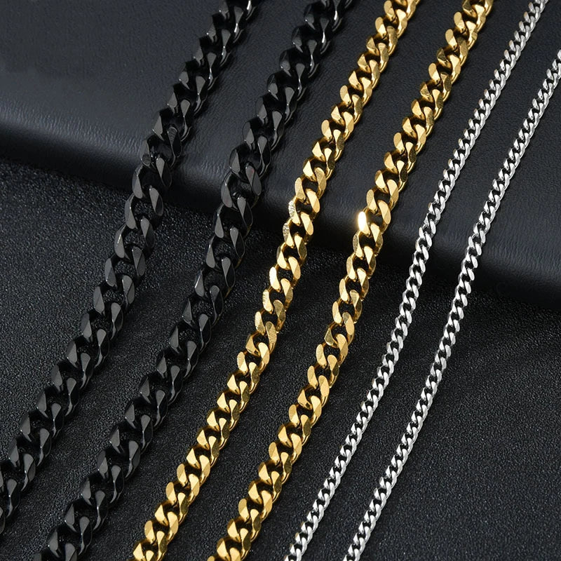 A close-up of four men's Cuban link chains in black, gold, and silver stacked on a dark surface.