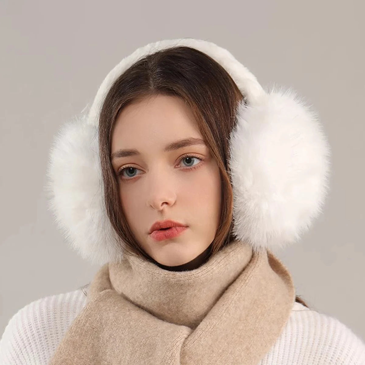 A woman wearing white knitted clothing and a beige faux fur scarf, with fluffy white faux fur earmuffs visible.